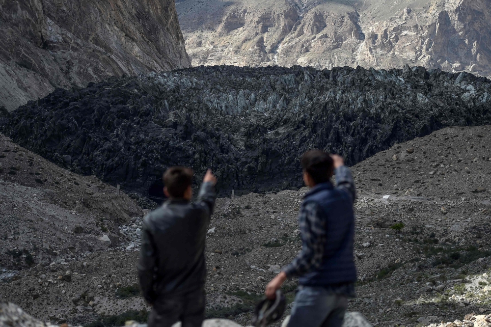 This picture taken on June 28, 2019 shows men pointing at the black Shisper glacier in the Karakoram mountain range of Pakistan's Gilgit-Baltistan region. AFP / Aamir Qureshi
