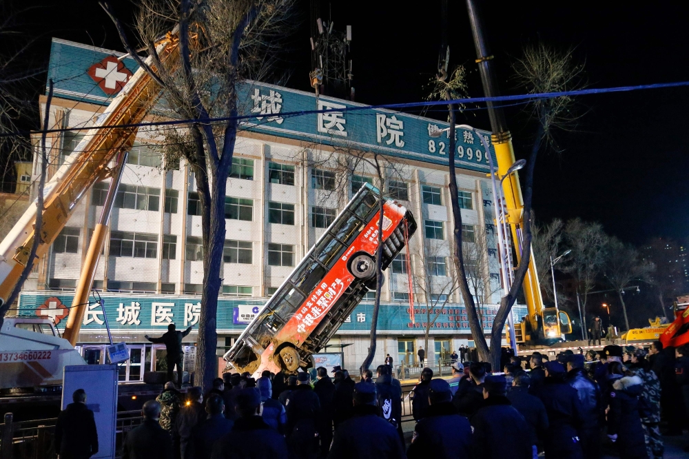 This photo taken on January 13, 2020 shows Chinese rescuers watching as a bus is lifted out after a road collapse in Xining in China's northwestern Qinghai province. An enormous sinkhole swallowed passers-by and a public bus in northwest China, reported s
