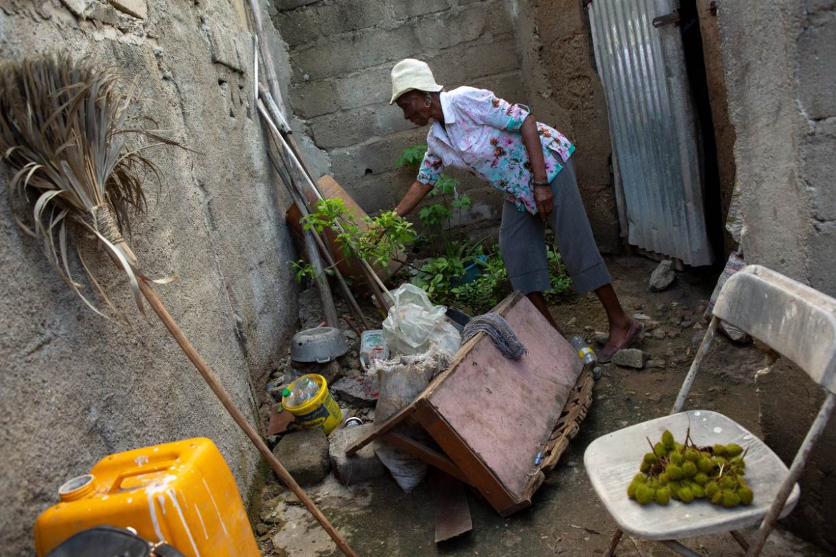 Farmer Rose Marie Fidele, 73, tends to the few plants she can coax to grow in a little urban space behind the home she shares with her son and his family near Caracol, Haiti, December 10, 2019. Handout by Allison Shelley