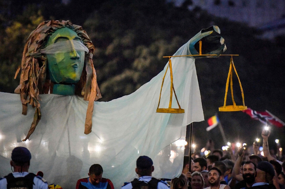 Romanians chant slogans next to a giant statue picturing the symbol of justice during a demonstration on August 11, 2018 in Bucharest. AFP / Daniel Mihailescu