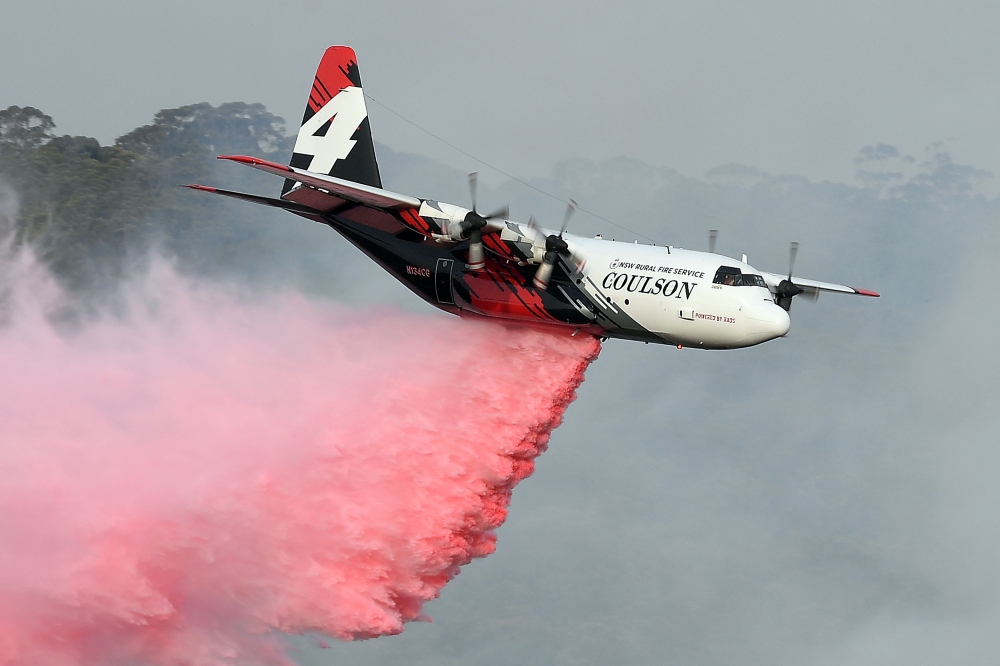 (FILES) This file photo taken on January 10, 2020 shows a C-130 Hercules plane from the New South Wales Rural Fire Service dropping fire retardent to protect a property during an operation to douse bushfires in Penrose, in Australia's New South Wales stat