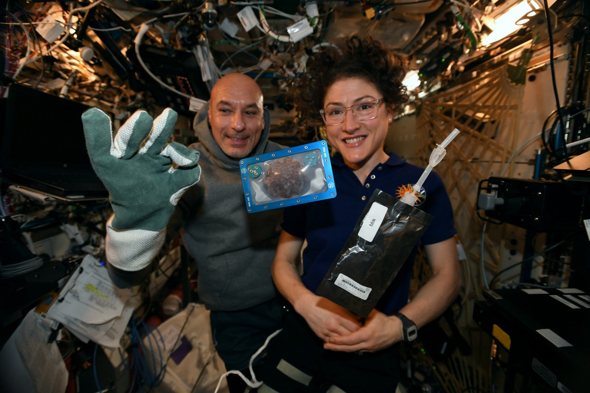 In this photo made available by U.S. astronaut Christina Koch and Italian astronaut Luca Parmitano pose for a photo with a cookie baked on the International Space Station Twitter: @Astro_Christina
