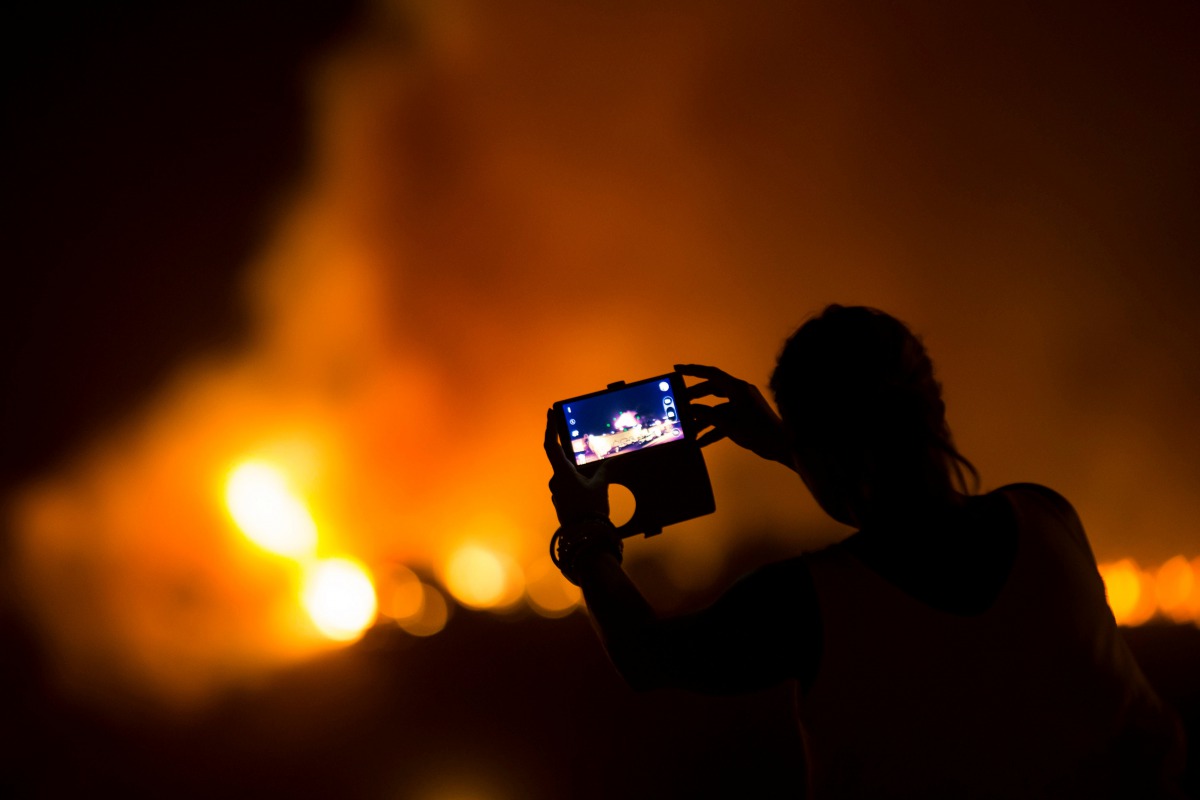 A woman uses her mobile phone to film as a forest fire burns out of control in Las Manchas on the southwestern part of La Palma island, Spain, August 5, 2016. Reuters / Borja Suarez