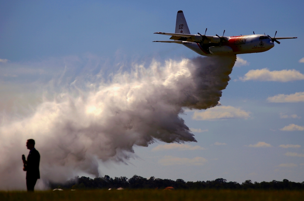 A television reporter stands in front of a Large Air Tanker (LAT) C-130 Hercules as it drops a load of around 15,000 litres during a display by the Rural Fire Service ahead of the bushfire season at RAAF Base Richmond Sydney, Australia, September 1, 2017.