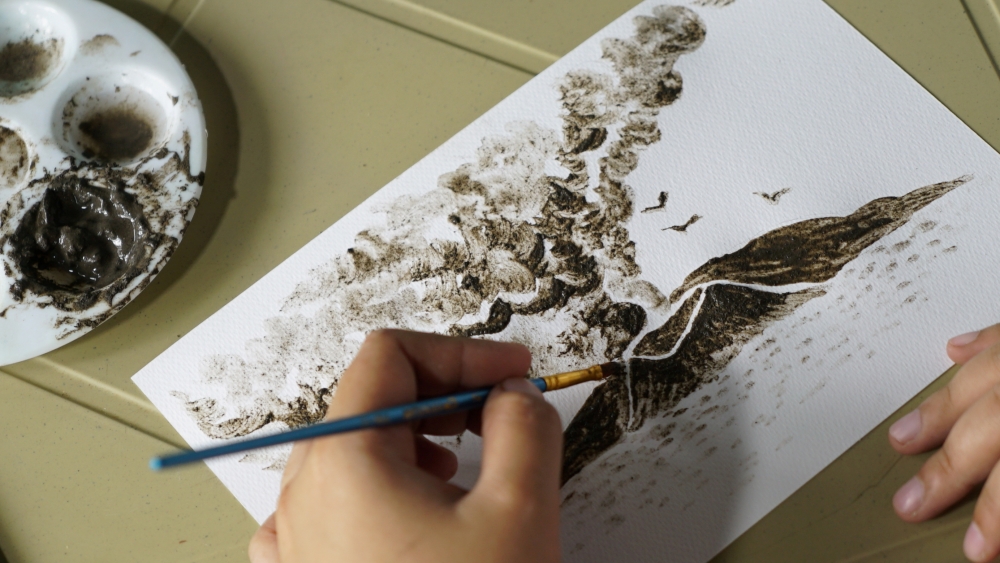 Filipina artist Janina Sanico paints an image of Taal volcano spewing ash clouds using ash that accumulated in her yard in Tanauan, Batangas Province, Philippines, January 24,2020. REUTERS/Joseph Campbell