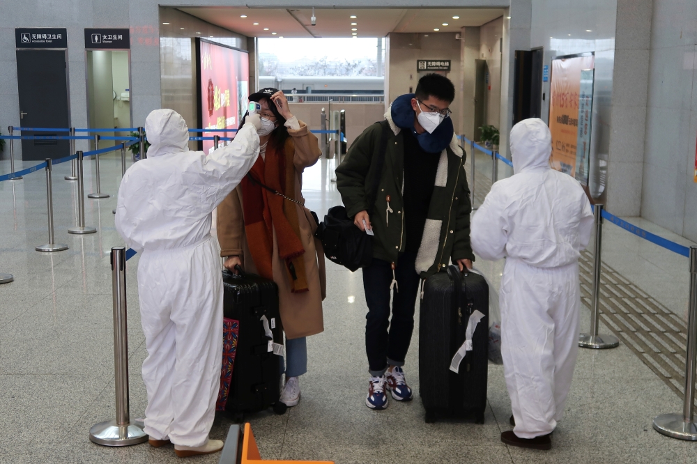 Workers in protective suits check the temperature of passengers arriving at the Xianning North Station on the eve of the Chinese Lunar New Year celebrations, in Xianning, a city bordering Wuhan to the north, in Hubei province, China January 24, 2020. REUT