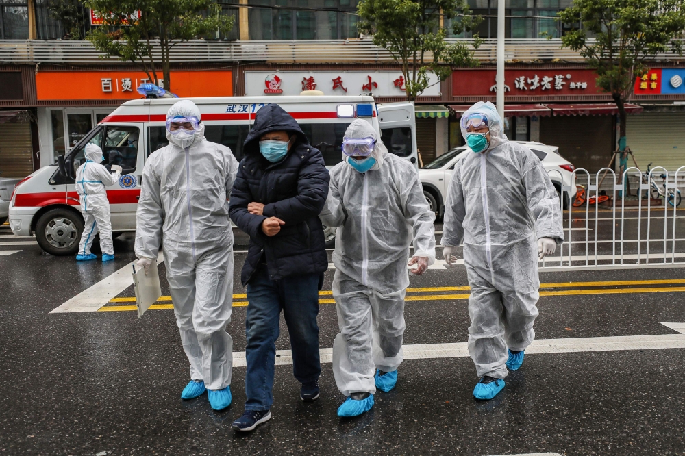 This photo taken on January 26, 2020 shows medical staff members wearing protective clothing to help stop the spread of a deadly virus which began in the city, accompanying a patient (2nd L) as they walk into a hospital in Wuhan in China's central Hubei p