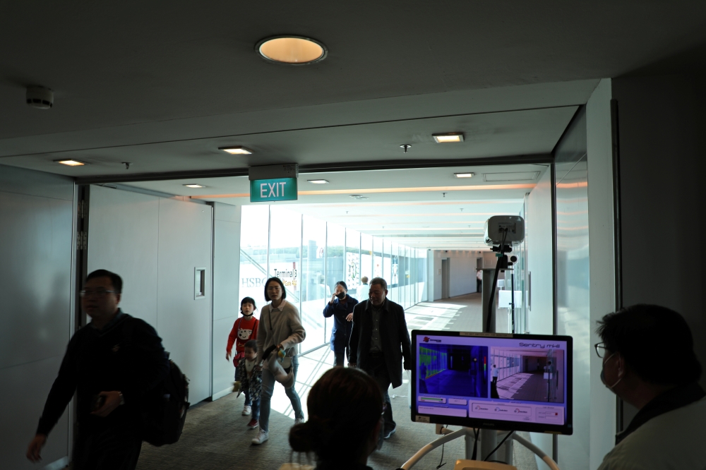 Officials monitor thermal scanners as passengers walk past upon arrival of a flight from Hangzhou, China at Changi Airport, Singapore January 22, 2020. REUTERS/Yiming Woo