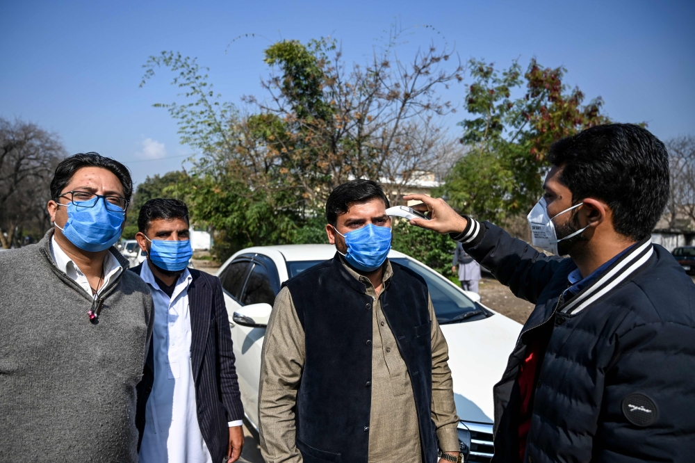 An official of Pakistan-based Chinese company (R) uses a thermo gun to check the temperature of the company's drivers, in Islamabad on January 30, 2020, after instructions from Pakistani authorities to take preventive measures against the coronavirus. A v
