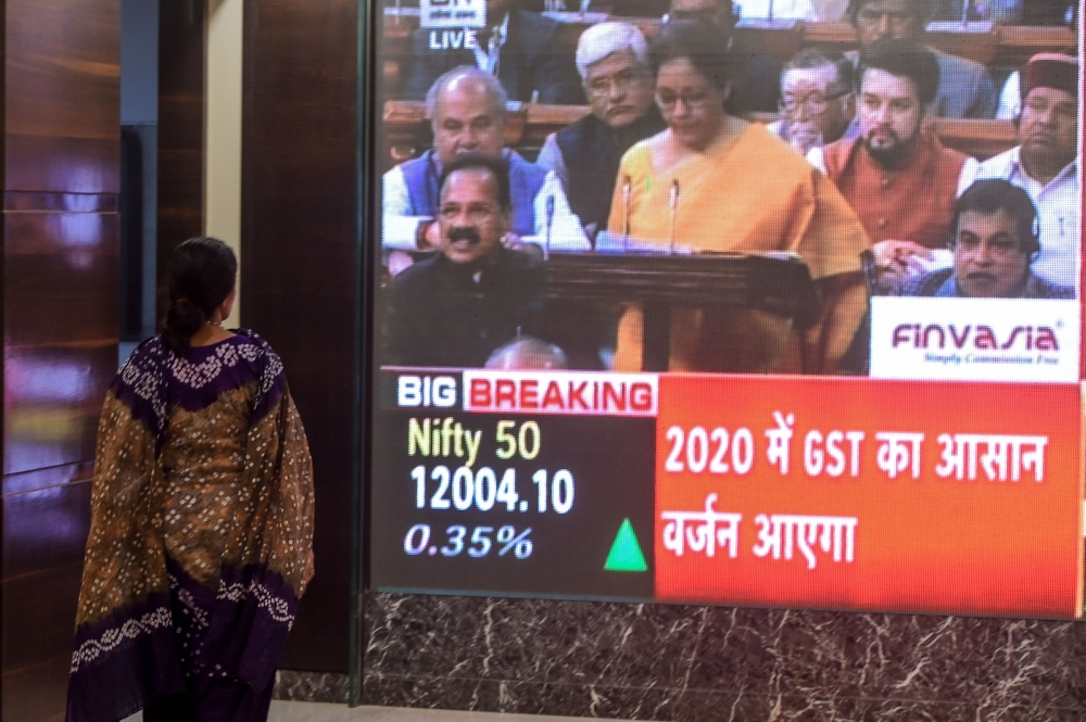 A woman stands as she watches a screen displaying a television channel live broadcast of India's Finance Minister Nirmala Sitharaman (C on screen) presenting the 2020 union budget, at the Bombay Stock Market (BSE) in Mumbai on February 1, 2020. (AFP / Pun