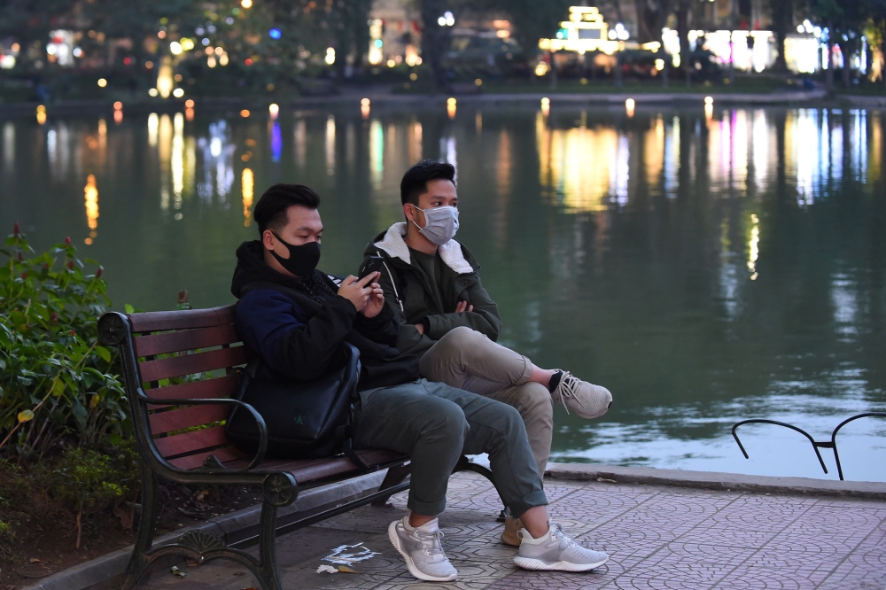 Two men wearing protective facemasks sit by the Hoan Kiem Lake in Hanoi on January 31, 2020. AFP / Nhac NGUYEN