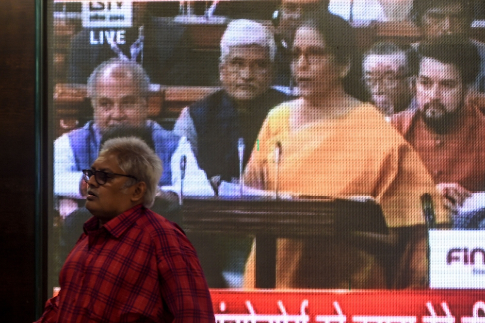 A man (L) walks past a screen displaying a television channel live broadcast of India's Finance Minister Nirmala Sitharaman (3R on screen) presenting the 2020 union budget at the Bombay Stock Market (BSE) in Mumbai on February 1, 2020. (AFP / Punit PARANJ