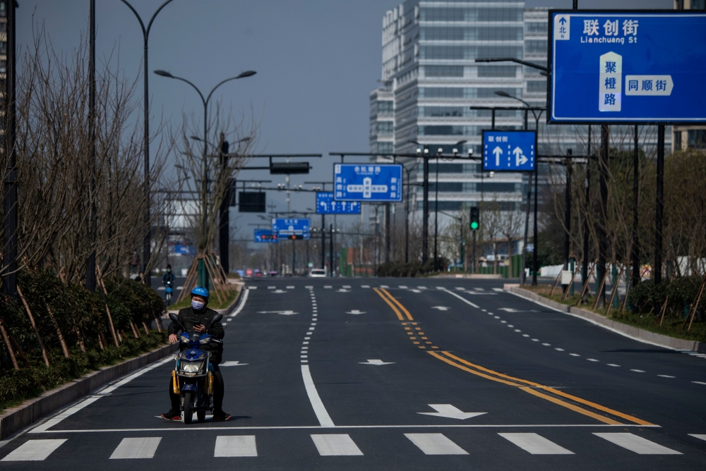 A lone motorcycle rider is seen on an empty street in Hangzhou, some 175 kilometres (110 miles) southwest of Shanghai on February 5, 2020, near the Alibaba headquarters.  AFP / NOEL CELIS