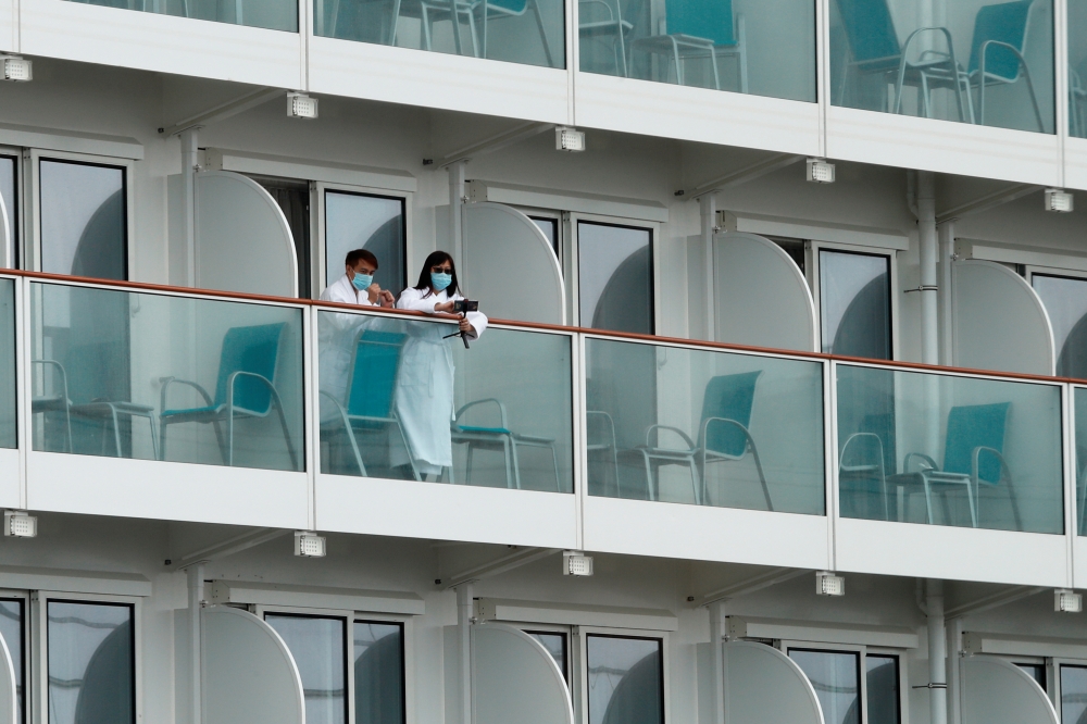 Passengers with face masks and bathrobes look out from a cabin of the World Dream cruise ship, after it had been denied entry in Taiwan amid concerns of coronavirus infection on board, at the Kai Tak Cruise Terminal in Hong Kong, China February 6, 2020. R