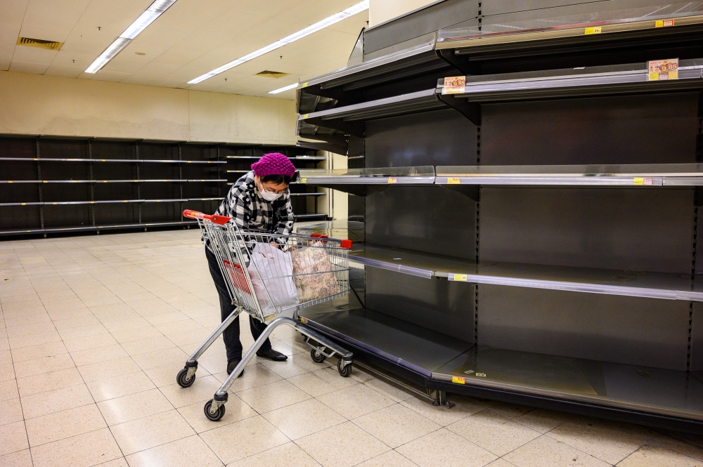 A shopper wearing a protective facemask sorts items in her trolley as she stands next to bare supermarket shelves, usually stocked with toilet paper and kitchen rolls, in Hong Kong on February 6, 2020. AFP / Philip Fong
