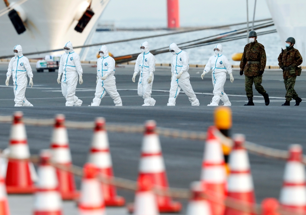 Workers and army officers wearing protective suits walk away from the cruise ship Diamond Princess, as they prepare to transfer passengers tested positive for the novel coronavirus, at Daikoku Pier Cruise Terminal in Yokohama, south of Tokyo, Japan Februa