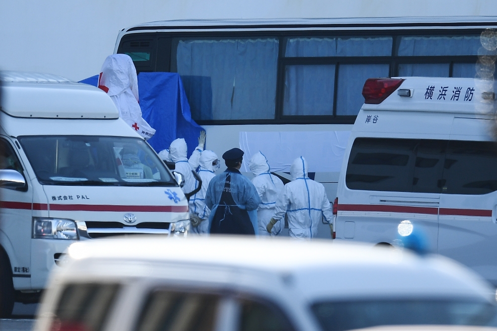 People wearing protective suits arrange a blue cover on a bus near the Diamond Princess cruise ship, with around 3,600 people quarantined onboard due to fears of the new coronavirus, at the Daikoku Pier Cruise Terminal in Yokohama port on February 11, 202