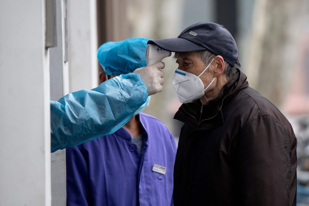 An elderly man wearing a face mask has his temperature checked before entering a community hospital in Shanghai on February 13, 2020. AFP / NOEL CELIS