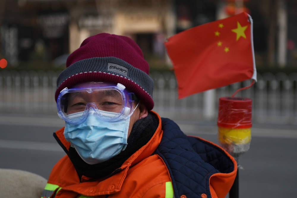 A cleaner wears a mask and goggles as he commutes on a street in Beijing on February 11, 2020.  / AFP / GREG BAKER
