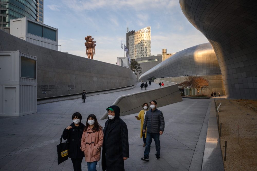 In a photo taken on February 11, 2020 people wearing face masks walk through Dongdaemun Design Plaza in Seoul. / AFP / Ed JONES 