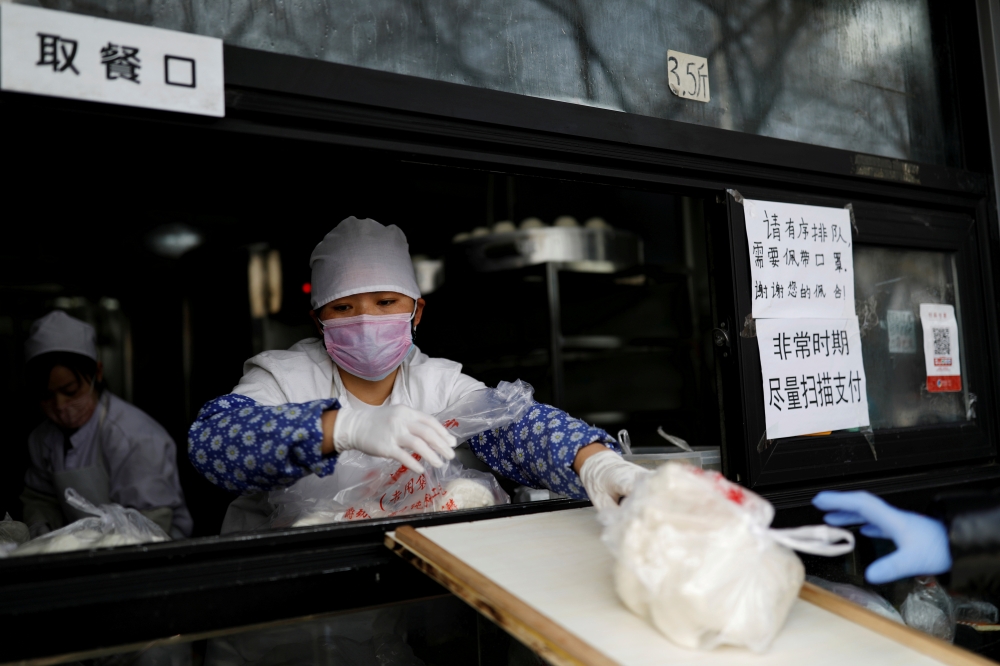 An employee deliver buns to a customer through a ramp from the restaurant counter at a store, as the country is hit by an outbreak of the novel coronavirus, in Beijing, China February 12, 2020. Reuters/Carlos Garcia Rawlins