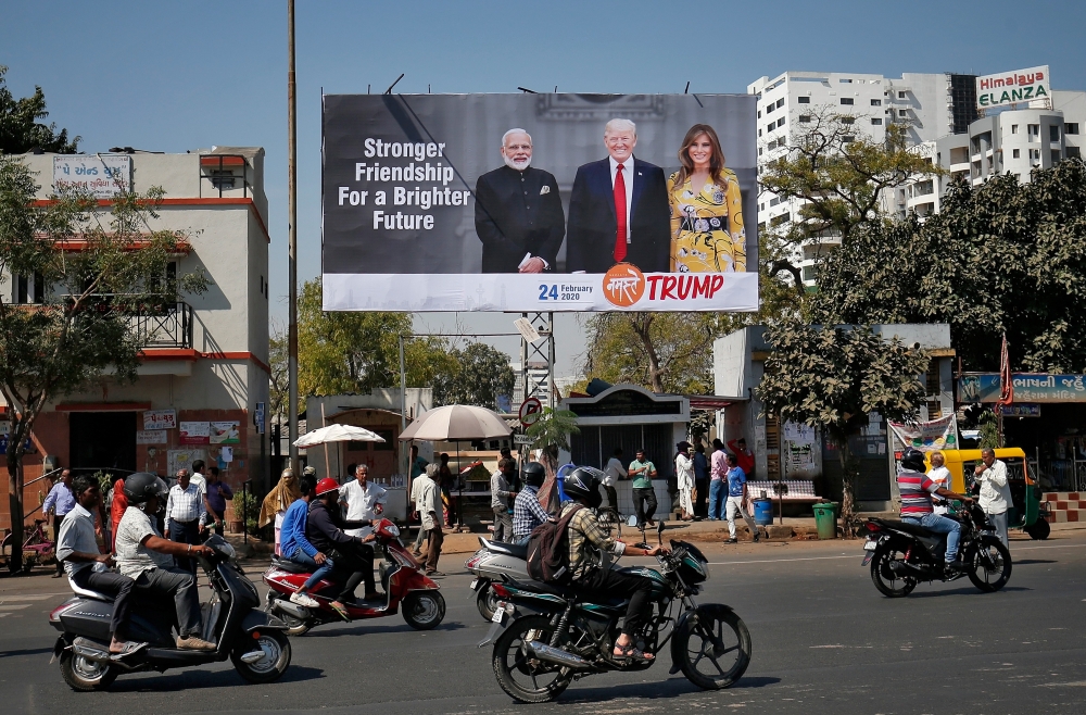 People ride their motorbikes past a hoarding with the images of India's Prime Minister Narendra Modi, U.S. President Donald Trump and first lady Melania Trump ahead of Trump's visit, in Ahmedabad, India, February 18, 2020. REUTERS/Amit Dave
 
