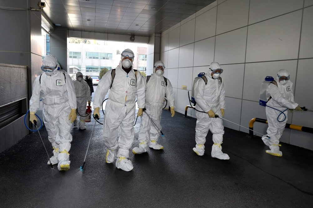 This picture taken on February 19, 2020 shows South Korean health officials wearing protective suit and spraying disinfectant near a church in the southeastern city of Daegu as about 40 new cases of the COVID-19 coronavirus confirmed after they attended s