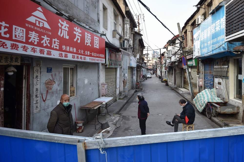 This photo taken on February 23, 2020 shows people standing on a street by a barrier to stop others from entering, in Wuhan in China's central Hubei province. / AFP / STR