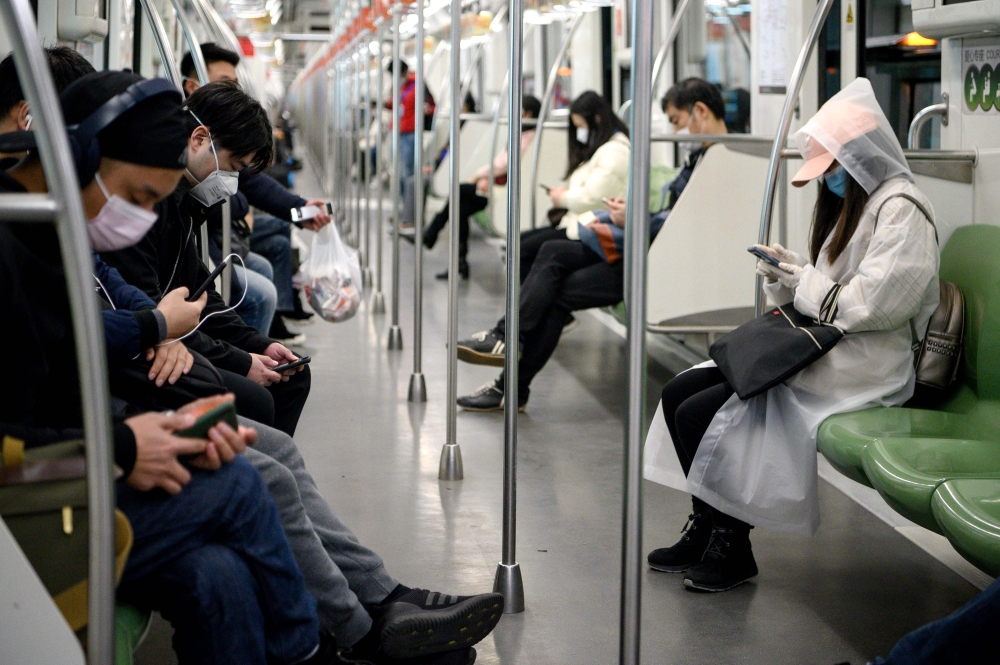 Passengers wearing protective face masks travel on the subway in Shanghai on February 25, 2020. China on February 25 reported another 71 deaths from the COVID-19 coronavirus, the lowest daily number of fatalities in over two weeks, which raised the toll t