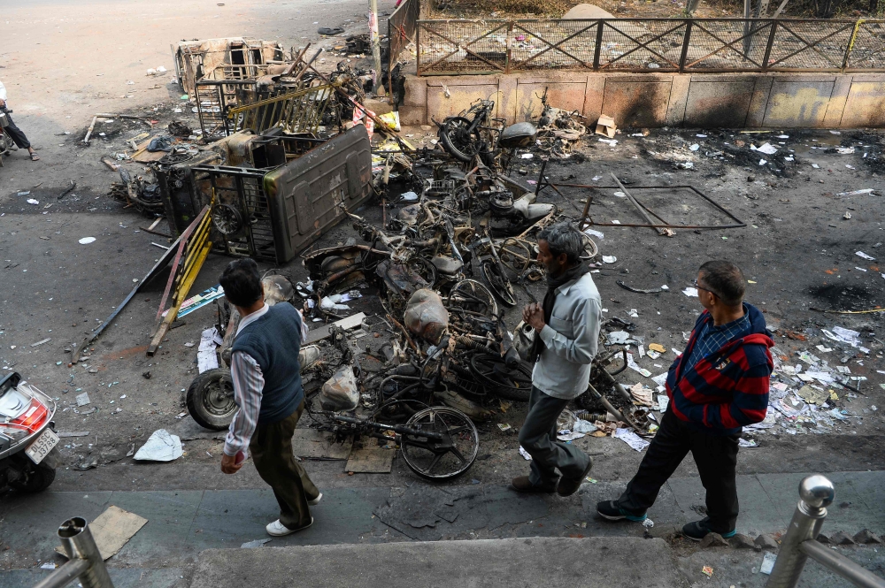 Men make their way around burnt-out vehicles following clashes between people supporting and opposing a contentious amendment to India's citizenship law, in New Delhi on February 26, 2020./ AFP / Sajjad HUSSAIN 