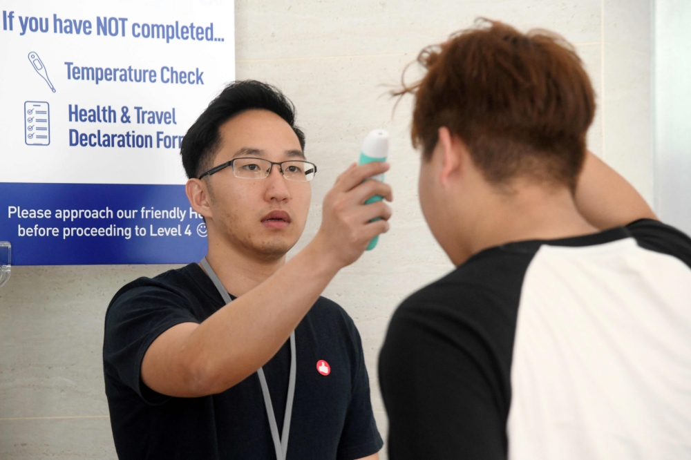 This photograph taken on February 22, 2020 shows a volunteer (L) taking a temperature of a church member attending a small group service as a protective measure to prevent the spread of the COVID-19 coronavirus in Singapore. AFP / Roslan RAHMAN