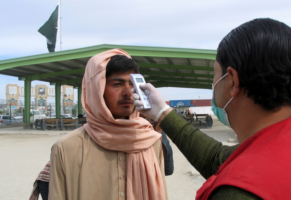 A health worker takes the temperature of a man, who returned from Afghanistan, for a medical observation as a preventive measure following the coronavirus outbreak, outside a medical camp set up near the Friendship Gate, crossing point at the Pakistan-Afg