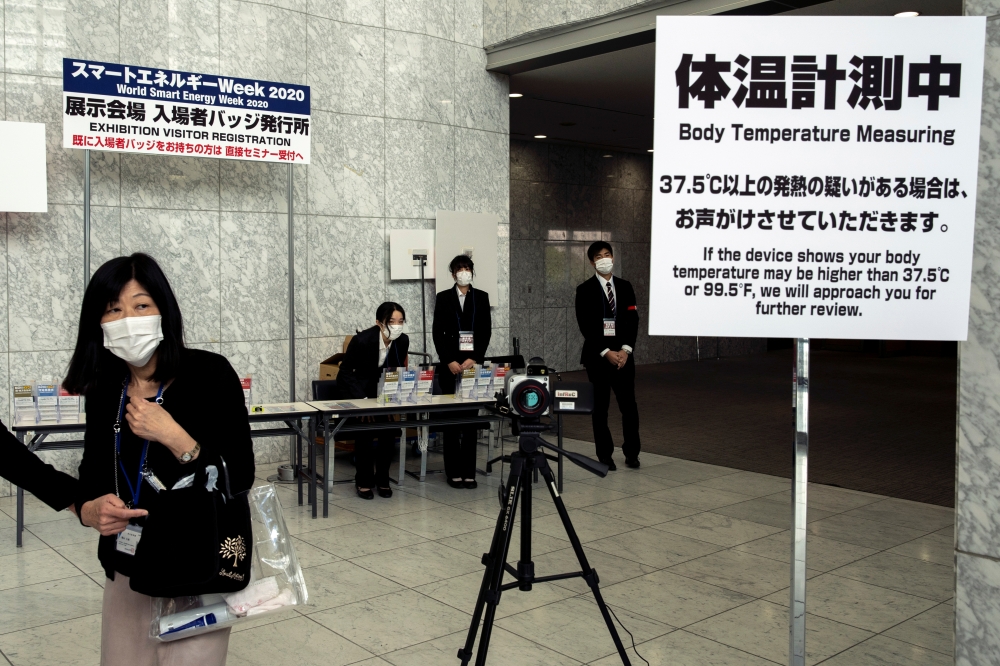 Workers wearing protective face masks, following an outbreak of the coronavirus, stand near a machine measuring body temperature at a convention hall in Tokyo, Japan, February 27, 2020. REUTERS/Athit Perawongmetha 
