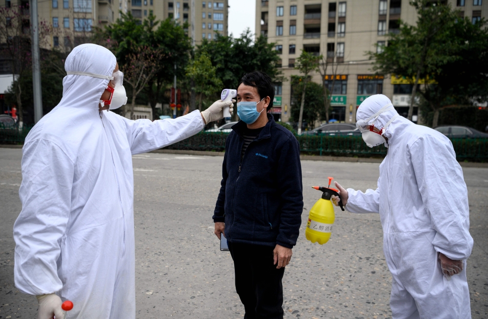 This photo taken on February 28, 2020, shows a factory employee being disinfected and his temperature taken by security guards in protective gear at the entrance of the Azure Eyeglasses Company in Wenzhou. FOCUS BY DAN MARTIN / AFP / NOEL CELIS /