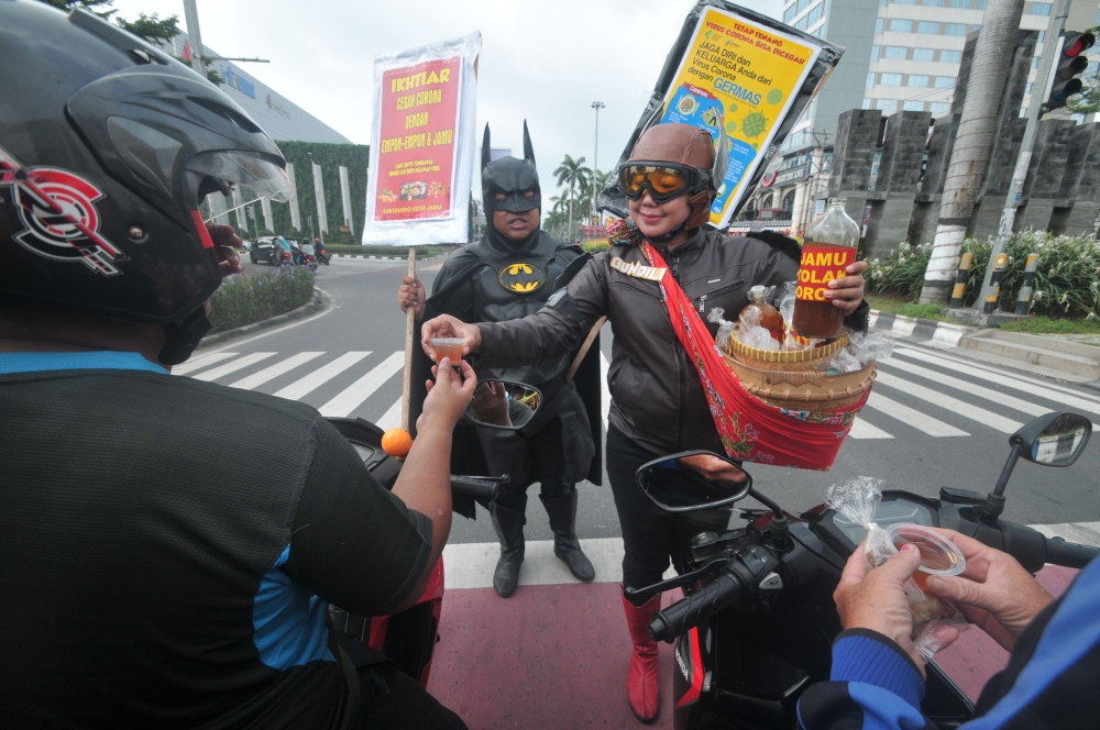 People wearing characters clothes of local hero Gundala (R) and Batman (L) offer Indonesian traditional herbal drinks “Jamu” to motorists as they encourage them to stay healthy and fight COVID-19 in Solo on March 4, 2020. / AFP / ANWAR MUSTAFA 