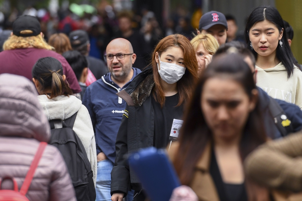 A woman wearing a face mask crosses the street in Melbourne on March 5, 2020. Over 50 people have been confirmed to have the COVID-19 coronavirus in Australia so far with the latest cases including an eight-month-old baby in Adelaide. / AFP / William WEST