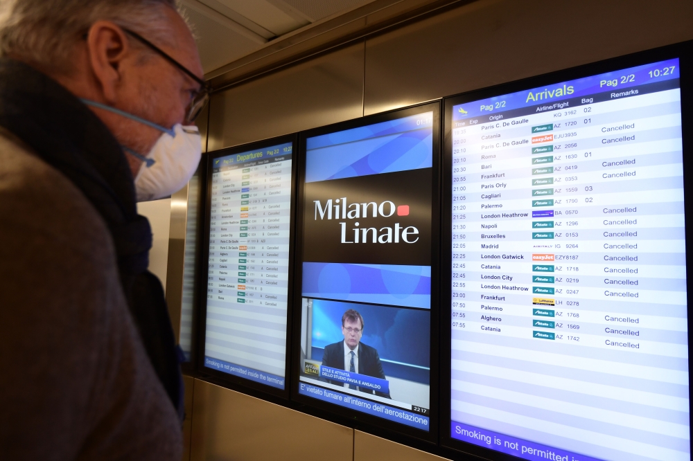 A passenger wearing a protective mask checks a flights timetable at Milan's Linate airport on March 11, 2020, a day after Italy imposed unprecedented national restrictions on its 60 million people Tuesday to control the deadly COVID-19 coronavirus. / AFP 