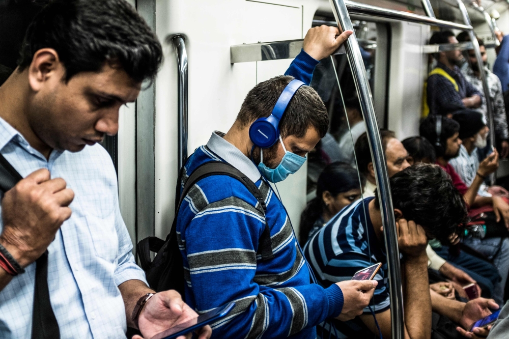 A commuter (C) wearing a facemask as a preventive measure against the spread of the COVID-19 coronavirus uses his phone while travelling on the Violet Line of the Delhi Metro, in New Delhi on March 12, 2020. / AFP / XAVIER GALIANA