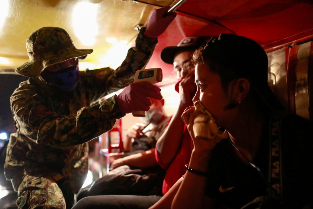 A police officer checks a jeepney passenger's body temperature at a checkpoint placed amidst the lockdown of the country's capital to contain the spread of coronavirus, in the outskirts of Quezon City, Metro Manila, Philippines, March 15, 2020. REUTERS/El