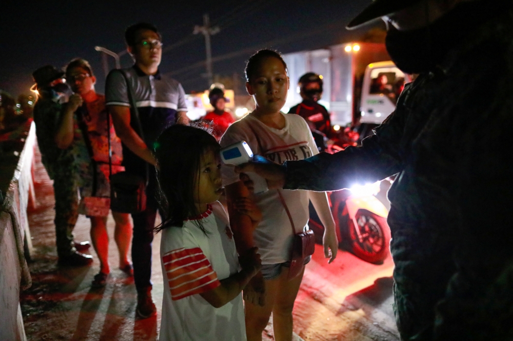 A girl holds on to her mother as a police officer checks her body temperature at a checkpoint placed amidst the lockdown of the country's capital to contain the spread of coronavirus, in the outskirts of Quezon City, Metro Manila, Philippines, March 15, 2