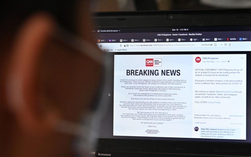 A man reads an announcement by CNN Philippines of their temporary closure from their facebook page, due to a positive COVID-19 infection at their building in Manila on March 18, 2020. / AFP / Ted ALJIBE