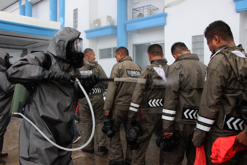 Officials from a police unit spray each other before performing disinfecting measures at the tourist area of Gili Trawangan on Lombok island on March 18, 2020, amid concerns of the COVID-19 coronavirus outbreak. / AFP / PIKONG