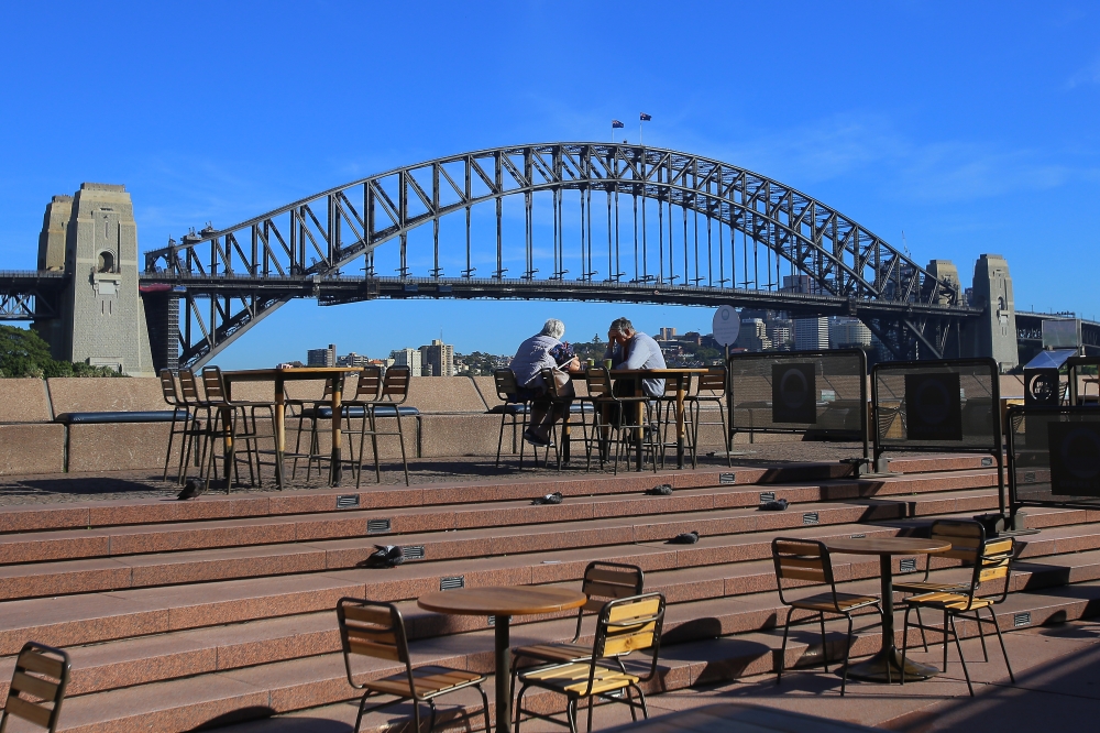 An elderly couple sit at a table in front of the Sydney Harbour Bridge, following an outbreak of coronavirus (COVID-19), in Sydney, Australia, on March 19, 2020. (Steven Saphore - Anadolu Agency)