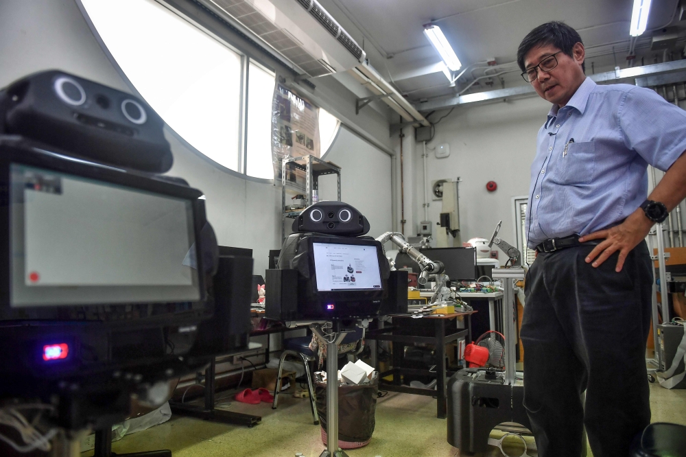 In this photo taken on March 18, 2020 professor Viboon Sangveraphunsri stands next to medical robots modified to screen and observe COVID-19 coronavirus patients at the Regional Center of Robotics Technology at Chulalongkorn University in Bangkok. AFP / L