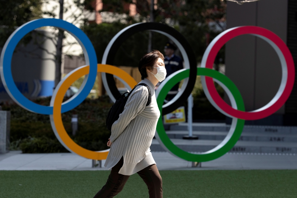 FILE PHOTO: A woman wearing a protective face mask, following an outbreak of the coronavirus disease (COVID-19), walks past the Olympic rings in front of the Japan Olympics Museum in Tokyo, Japan March 13, 2020. REUTERS/Athit Perawongmetha