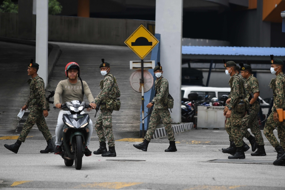 A motorcyclist rides past soldiers inside a police station during the control of movement in Kuala Lumpur on March 22, 2020, amid fears over the spread of the COVID-19 novel coronavirus. / AFP / Mohd RASFAN
