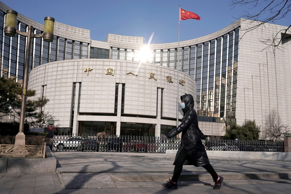 FILE PHOTO: A woman wearing a mask walks past the headquarters of the People's Bank of China, the central bank, in Beijing, China, as the country is hit by an outbreak of the new coronavirus, February 3, 2020. REUTERS/Jason Lee/File Photo