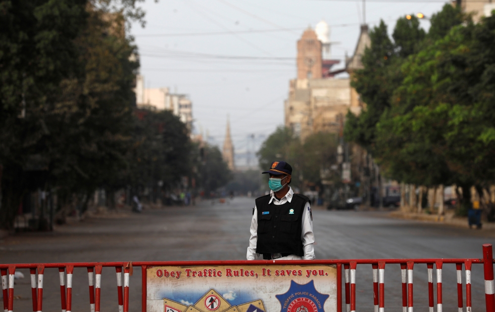 A traffic police officer stands with a barrier on a deserted road of a business district during a partial lockdown after Pakistan shut all markets, public places and discouraged large gatherings amid an outbreak of coronavirus disease (COVID-19), in Karac