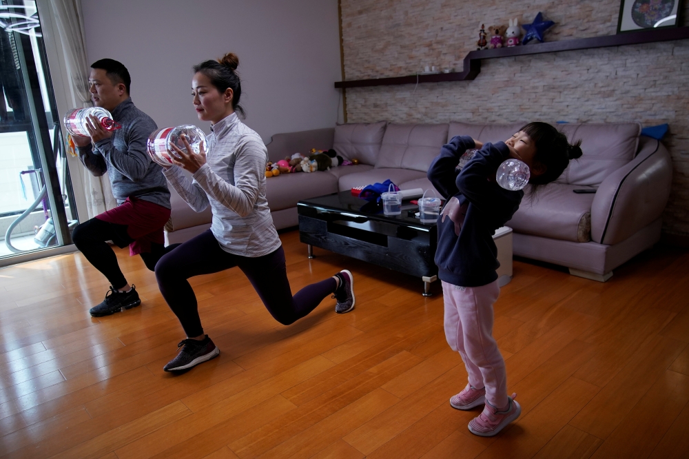 Dino Lin, Stella Zhang and Wowo Lin, 5, exercise using filled water bottles as weights as they watch a fitness class online at their house, during the novel coronavirus disease (COVID-19) outbreak, in Shanghai, China, February 25, 2020. Reuters/Aly Song 