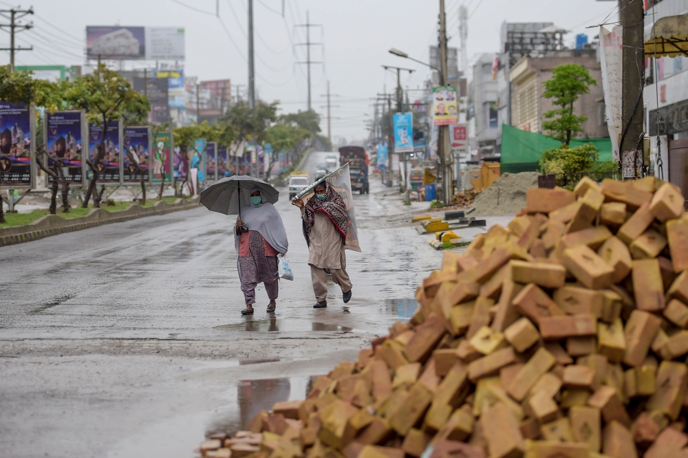 Two women wearing facemasks walk unrder the rain during a government-imposed lockdown as a preventive measure against the COVID-19 coronavirus in Islamabad on March 24, 2020. / AFP / Farooq NAEEM
